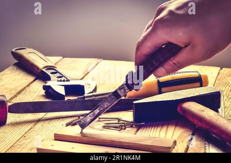 Handhaltewerkzeug in der Werkstatt. Schraubendreher, Flachfeile, Zange, Affenschlüssel, Schrauben und Dielen auf natürlichem Holzhintergrund. Stockfoto
