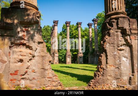 Brüchiges Ziegel- und Stuckmauerwerk steht im Vordergrund, während sich eine Reihe von Säulen auf einem sonnenbeschienenen Rasen dahinter befindet, bei den Windsor Ruins, Mississippi. Stockfoto