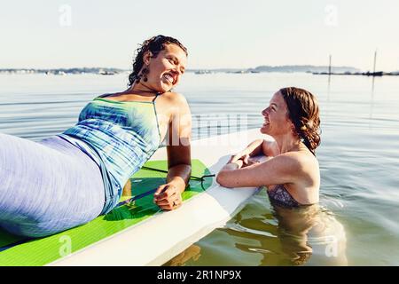 Zwei junge Freundinnen entspannen sich auf dem Stehpaddelbrett in Casco Bay Stockfoto