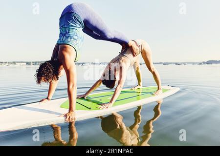 Zwei junge Frauen, die Yoga auf einem Stehpaddelbrett machen Stockfoto