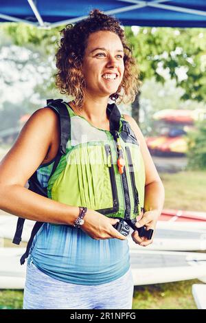 Junge Frau zieht ihre Schwimmweste an, um sich auf den Kajakausflug vorzubereiten Stockfoto