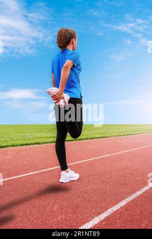 Sportlerin steht vor dem Start auf der Laufbahn und wärmt sich vor dem Lauf auf, reißt das Bein. Stockfoto