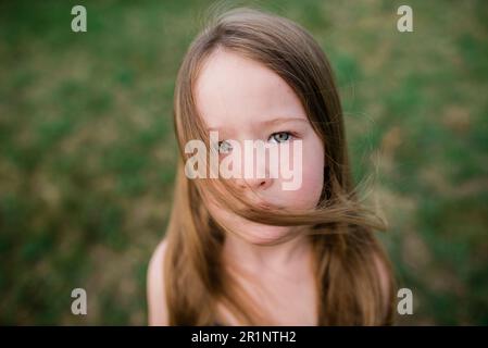 Nahaufnahme eines ernsthaften Mädchens im Gras, das sich die Haare vom Kamerawind ansieht Stockfoto