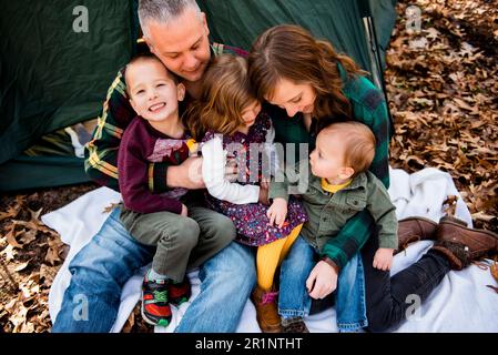 Lächelnde Familie sitzt auf einer Decke außerhalb des Zelts im Herbst und umarmt sich Stockfoto