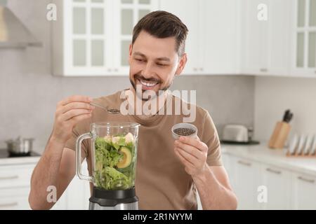 Glücklicher Mann, der Chiasamen in den Mixer mit Zutaten für Smoothie in der Küche gab Stockfoto