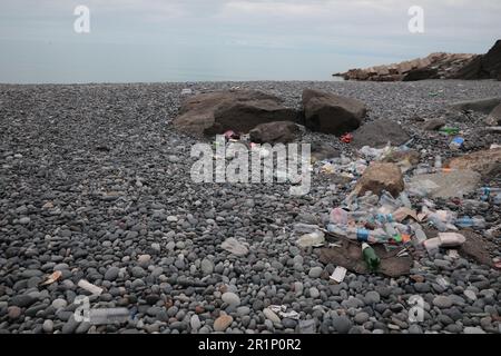 Müll verstreut auf Kieselsteinen nahe dem Meer. Recycling-Problem Stockfoto