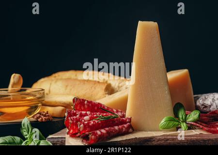 Köstlicher Parmesankäse, Wurstscheiben, Honig, Brot und Basilikum auf Holzbrett, Nahaufnahme Stockfoto