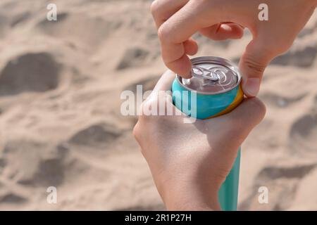 Frau öffnet Aluminiumdose mit Getränk auf Sand, Nahaufnahme. Platz für Text Stockfoto