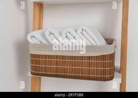 Weiche Handtücher in Korb aus Korb auf dekorativer Leiter nahe der weißen Wand Stockfoto
