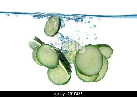 Frische Gurkenscheiben, die auf weißem Hintergrund ins Wasser fallen, Nahaufnahme Stockfoto