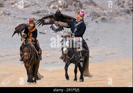 Kasachische Jäger auf dem Pferderücken, mit Kapuzen-Goldenen Adlern (Aquila chrysaetos), auf dem Weg zum Eagle Hunters Festival, Bayan-Ulgii, westliche Mongolei Stockfoto