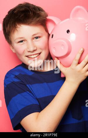 Glücklicher Junge, Porträt und Sparschwein mit Lächeln für Ersparnisse, Geld oder Münzen vor einem pinkfarbenen Studiohintergrund. Ein kleines Kind oder Kind mit einem Huckepack und Stockfoto