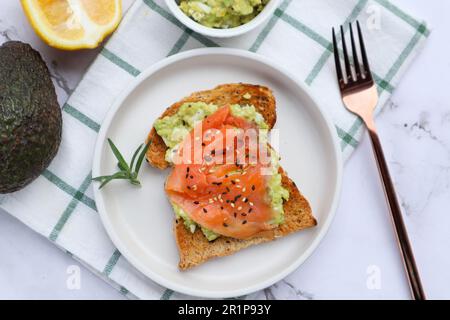 Toast mit Avocado und geräuchertem Lachs mit Sesamsamen oben auf dem Marmortisch - gesundes Essen Stockfoto