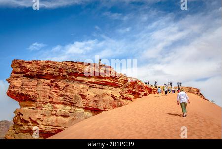 Touristen haben Spaß beim Klettern auf eine Düne in der Wüste von Wadi Rum in Jordanien. Stockfoto