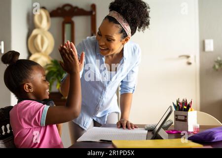 Glückliche afroamerikanische Mutter High Five mit Tochter, die zu Hause mit einem Tablet Schularbeiten macht Stockfoto