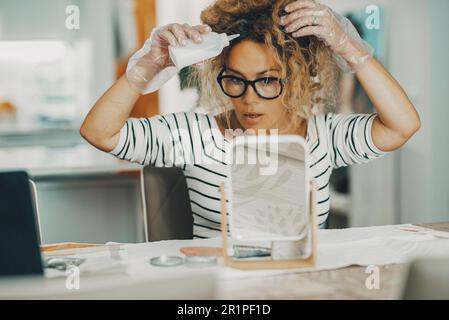 Beauty Care diy at Home Konzept Lifestyle. Selbständige Frau, die Haare mit Creme färbt oder pflegt. Freizeitaktivitäten im Friseurstil, weibliche Gäste sitzen am Tisch im Apartment. Das natürliche Leben Stockfoto