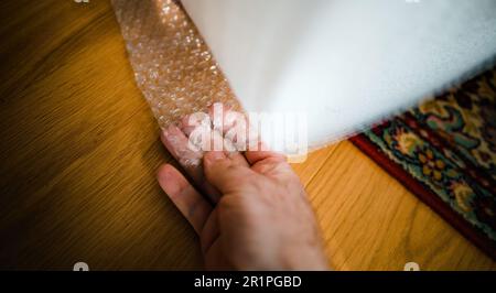 Ein Mann testet eine große Rolle Luftblasen-Verpackungsfolie, die das Konzept des sicheren und sicheren Warentransports vermittelt. Stockfoto