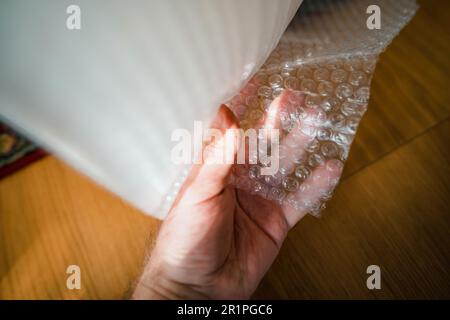 Ein Mann testet sorgfältig eine riesige Rolle Luftblasen-Verpackungsfolie, die die Bedeutung eines sicheren Transports von Waren zeigt. Stockfoto
