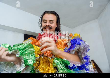 Junge Latino-Person mit nicht binärem Geschlecht und Drag Queen, die ihr Kleid fertigstellt, um zum Pride march zu gehen, sie ist glücklich, lächelnd, sehr aufgeregt. Stockfoto