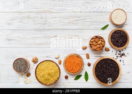 Verschiedene Superfoods in der kleinen Schüssel auf farbigem Hintergrund. Superfood wie Reis, Chia, Quinoa, Linsen, Nüsse, Sesamsamen, Mandeln. Kopierbereich der Draufsicht. Stockfoto