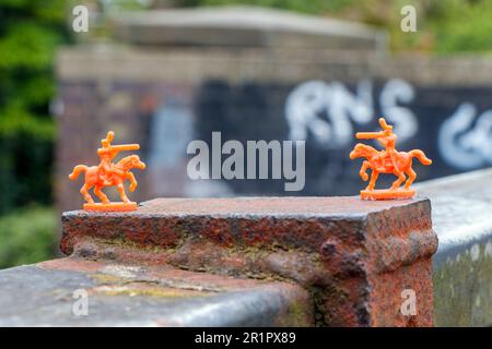 Orangefarbene Miniatur-Spielzeugsoldaten, die auf dem Parkland Walk in North London, Großbritannien, an einer Brücken-Attika kleben Stockfoto