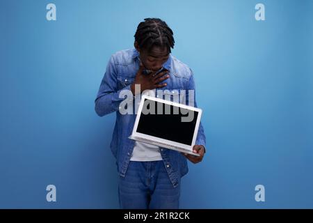 Ein amerikanischer Mann mit Dreadlocks in einer Jeansjacke arbeitet aus der Ferne mit einem Laptop Stockfoto