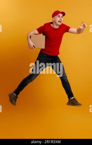 Liefermann mit roter Mütze, T-Shirt mit Pappkarton und Sprung Stockfoto