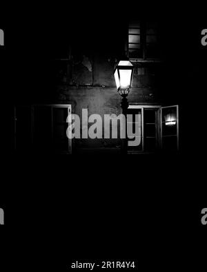 Eine Straßenlampe, die in der Dunkelheit vor dem Hintergrund von Fenstern leuchtet. Stockfoto