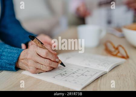 Nahaufnahme einer Seniorin, die ein Kreuzworträtsel macht. Stockfoto