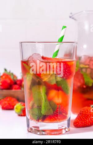 Hausgemachte Erdbeerlimonade in Krug und Glas, mit vielen zerstoßenem Eis, geschnittenen Beeren und Minzblättern, gefrorenen Erdbeeren Sangria, Eistee, Punsch o Stockfoto