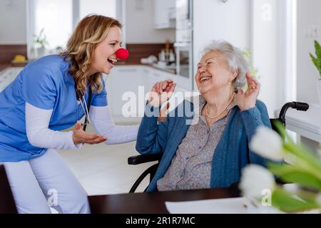 Eine Schwester mit Clownnnase, die Spaß mit ihrer Seniorin-Klientin hat. Stockfoto