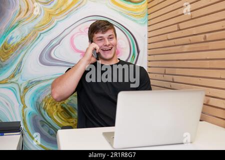 Junger männlicher Student sitzt in einer Privatzelle auf dem College Campus und telefoniert Stockfoto