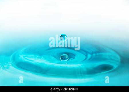 Wassertropfen fallen dicht in das blaue Wasser, was es zum perfekten Zentrum in der Natur macht Stockfoto