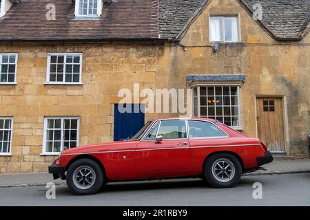 Chipping Campden, Großbritannien - August 2022; Seitenansicht eines hellroten Triumph Spitfire GT mit typischen gelben Kalksteinhäusern der Cotswolds als Kulisse Stockfoto