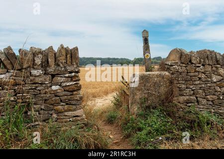 Broadway, UK-August 2022; Nahaufnahme der Öffnung in Kalkstein-Trockenmauern und Beschilderung des öffentlichen Fußwegs Cotswolds Way auf einem landwirtschaftlichen Feld Stockfoto