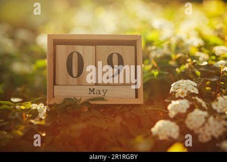 Holzblöcke mit dem Kalenderdatum vom 9. Mai inmitten von Blumen Stockfoto