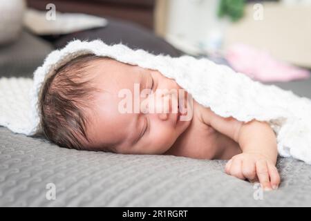 Glückliches Latina-Baby, das auf einem Bett mit einer weißen Decke lächelt Stockfoto