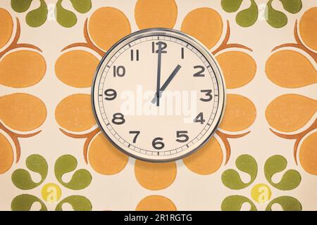 Die Bürouhr zeigt ein Uhr und hängt an einer Wand mit einer alten Tapete mit Blumenmuster Stockfoto