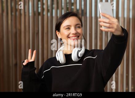 Fröhliche Sportlerin aus europa, die Selfie am Telefon macht, Friedenszeichen mit der Hand Stockfoto