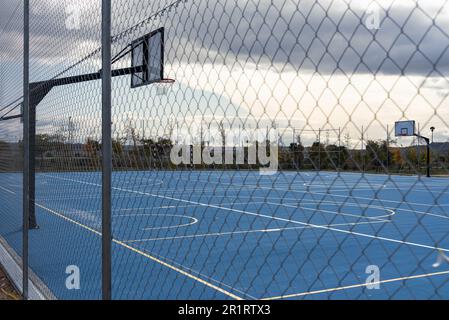 Blauer Basketballplatz im Freien hinter einem Zaun Stockfoto