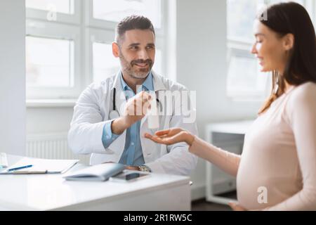 Schwangerschafts-Wellness. Junge schwangere Frau besucht männlichen Arzt, Therapeut, der Vitamine oder Nahrungsergänzungsmittel gibt Stockfoto