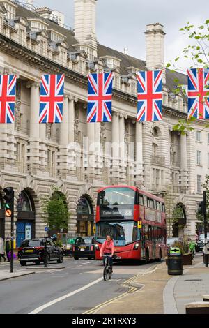 London, Großbritannien - 9. Mai 2023; Radfahrer und roter Londoner Bus auf der Regent Street mit suspendierten Union Jack Flaggen Stockfoto