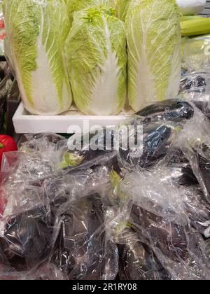 Eine Menge Chinakohl und Auberginen in Plastiktüten auf der Theke des Gemüsemarktes, vertikal Stockfoto