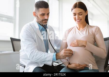 Gesundheit der schwangeren Frau und des Babys. Männlicher Arzt hört Babyherz während der Verabredung der jungen Dame im Krankenhaus Stockfoto