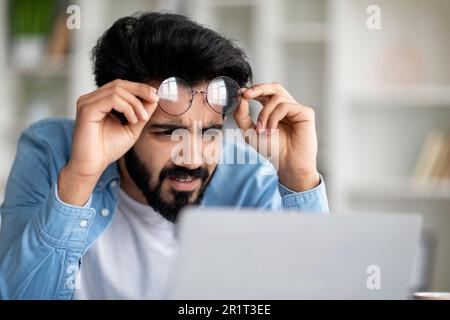 Fehler. Ein Verwirrter Indianer, Der Auf Einen Laptop Schaut Und Eine Brille Abnimmt Stockfoto