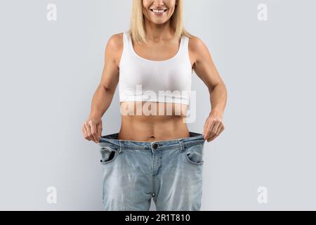 Eine nicht wiedererkennbare Frau mittleren Alters, die Entgiftungsergebnisse zeigt, große Jeans trägt Stockfoto