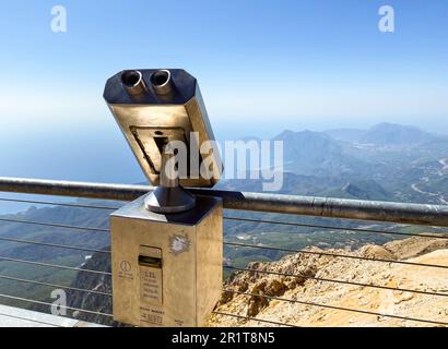 Fernglas auf einer Aussichtsplattform aus grauem Metall. Besichtigungstour, Beobachtung der Aussicht von den Bergen hinunter. Neben dem Fernglas ein Profi Stockfoto