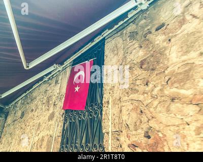 Wand in einem Wohngebiet. Eine rote Flagge der türkei ist auf einer Sperrholzplatte angebracht. Neben einem gebogenen Metallgitter. Stockfoto