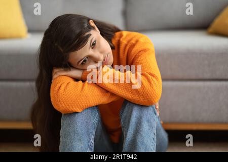 Frustrierte junge indianerin, die zu Hause auf dem Boden saß Stockfoto