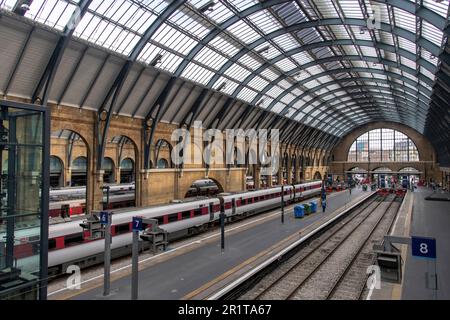 London, England - August 2022; Blick über die Bahnsteige mit wartenden Zügen und Passagieren in der Station Kings Cross in der Architektur der gotischen Wiedergeburt Stockfoto